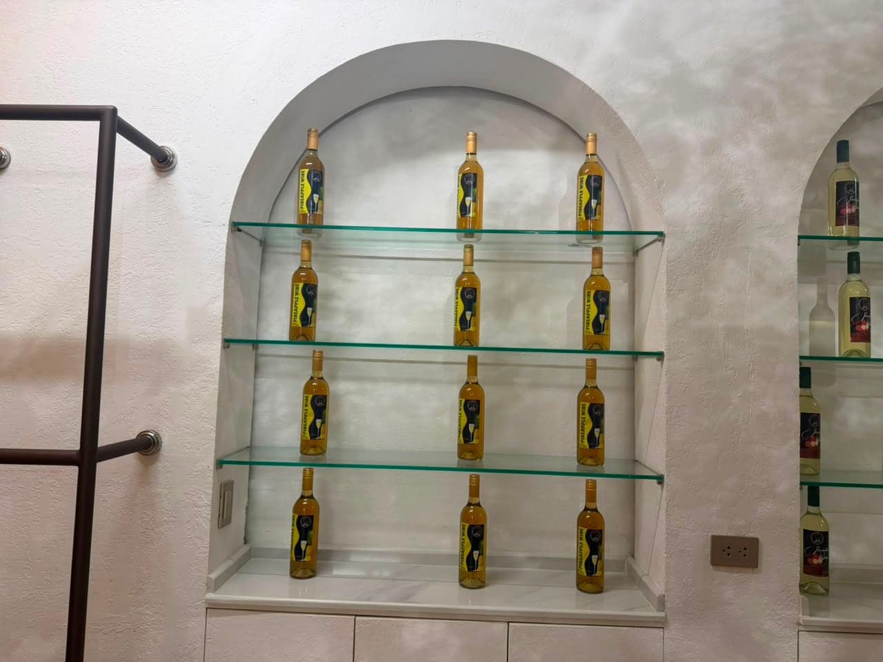 Bottles of ANA Pineapple Wine on glass shelves in an arched niche